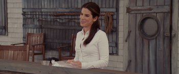 Movie still from “The Proposal” (2009), directed by Anne Fletcher – A woman sitting at a table in front of a wooden wall; Medium shot, Over the shoulder angle