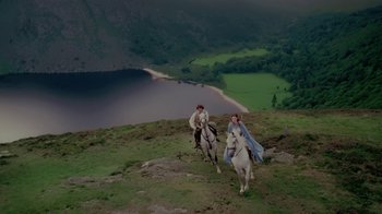 Movie still from “Ella Enchanted” (2004), directed by Tommy O'Haver – Two people riding horses on a hill near a body of water; Extreme Wide shot, High angle