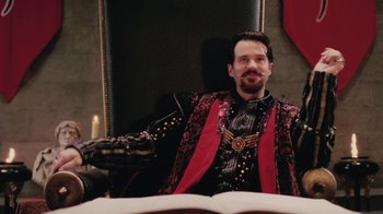 Movie still from “Ella Enchanted” (2004), directed by Tommy O'Haver – A man sitting in a chair wearing a red and black outfit; Medium shot, High angle