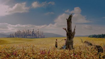 Two people in a field near a tree with a city in the background