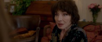 Movie still from “Elle” (2016), directed by Paul Verhoeven – An older woman sitting in a chair looking at the camera; Close Up shot, Over the shoulder angle