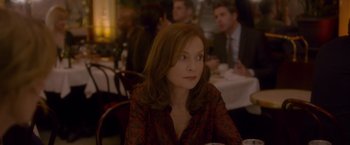 Movie still from “Elle” (2016), directed by Paul Verhoeven – A woman sitting at a table in front of a group of people; Close Up shot, Over the shoulder angle