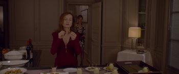 Movie still from “Elle” (2016), directed by Paul Verhoeven – A woman in a red dress eating a piece of cake; Medium shot, Over the shoulder angle