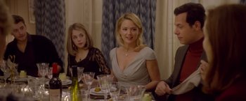 Movie still from “Elle” (2016), directed by Paul Verhoeven – A woman sitting at a dinner table with two other people; Medium shot, Over the shoulder angle