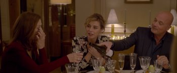 Movie still from “Elle” (2016), directed by Paul Verhoeven – A woman sitting at a table with a wine bottle; Medium shot, Over the shoulder angle