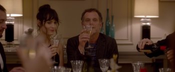 A man holding a wine glass in front of a woman sitting at a dinner table