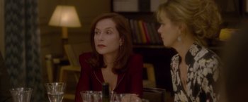 Movie still from “Elle” (2016), directed by Paul Verhoeven – A woman sitting at a table with another woman in the background; Close Up shot, Over the shoulder angle