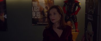 Movie still from “Elle” (2016), directed by Paul Verhoeven – A woman standing in front of a movie poster in a room; Medium shot, Over the shoulder angle