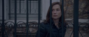 Movie still from “Elle” (2016), directed by Paul Verhoeven – A woman standing behind a metal fence looking at the camera; Close Up shot, Low angle