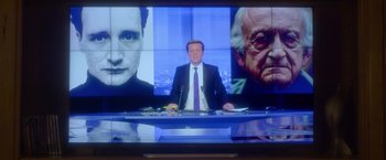 Movie still from “Elle” (2016), directed by Paul Verhoeven – A man in a suit and tie sitting in front of a tv; Extreme Close Up shot, Over the shoulder angle