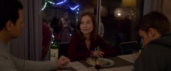 Movie still from “Elle” (2016), directed by Paul Verhoeven – A woman sitting at a table with a glass of wine; Medium shot, Over the shoulder angle