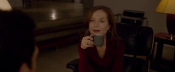 Movie still from “Elle” (2016), directed by Paul Verhoeven – A woman sitting in a chair holding a coffee mug; Close Up shot, Over the shoulder angle