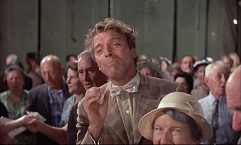 Movie still from “Elmer Gantry” (1960), directed by Richard Brooks – A man in a suit and bow tie blowing a kiss to the camera; Medium shot, Low angle