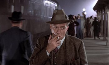 Movie still from “Elmer Gantry” (1960), directed by Richard Brooks – A man smoking a cigarette while standing on a sidewalk; Medium shot, Low angle