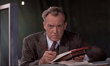 Movie still from “Elmer Gantry” (1960), directed by Richard Brooks – A man in a suit and tie writing on a book; Close Up shot, Low angle