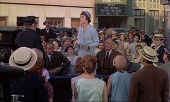 Movie still from “Elmer Gantry” (1960), directed by Richard Brooks – A woman in a blue dress standing in front of a group of people; Wide shot, Over the shoulder angle