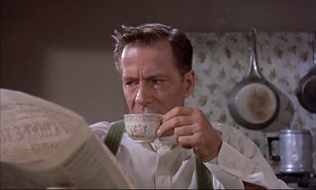 Movie still from “Elmer Gantry” (1960), directed by Richard Brooks – A man drinking a cup of coffee while reading a book; Close Up shot, Low angle