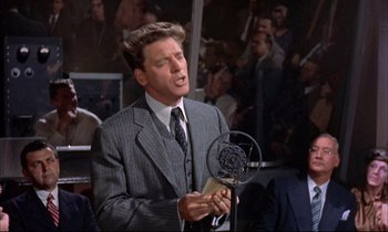 Movie still from “Elmer Gantry” (1960), directed by Richard Brooks – A man wearing a suit and tie holding a microphone; Medium shot, Low angle