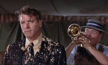 Movie still from “Elmer Gantry” (1960), directed by Richard Brooks – A man in a suit and tie with confetti all over his face; Medium shot, Over the shoulder angle