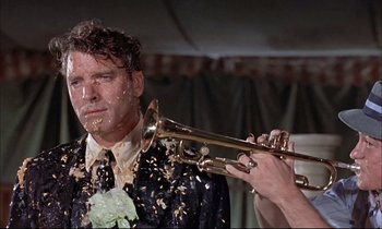 Movie still from “Elmer Gantry” (1960), directed by Richard Brooks – A man in a suit and tie with confetti on his face and a trumpet; Close Up shot, Over the shoulder angle