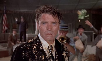 Movie still from “Elmer Gantry” (1960), directed by Richard Brooks – A man in a suit and tie and a trumpet; Medium shot, Over the shoulder angle