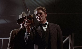 Movie still from “Elmer Gantry” (1960), directed by Richard Brooks – A man in a suit and hat holding a bottle of alcohol; Medium shot, Low angle