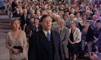 Movie still from “Elmer Gantry” (1960), directed by Richard Brooks – A man in a suit and tie standing in front of a group of people; Medium shot, Low angle