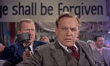 Movie still from “Elmer Gantry” (1960), directed by Richard Brooks – A man in a suit and tie holding a camera; Medium shot, Over the shoulder angle