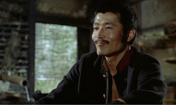 Movie still from “Empire of Passion” (1978), directed by Nagisa Ôshima – A man sitting in a chair smiling at the camera; Close Up shot, Low angle