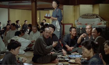Movie still from “Empire of Passion” (1978), directed by Nagisa Ôshima – A group of people sitting on the ground eating food; Wide shot, High angle