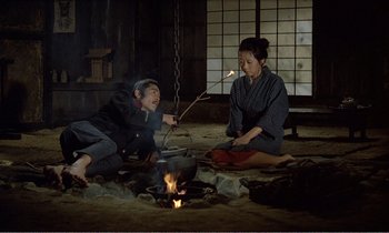 Movie still from “Empire of Passion” (1978), directed by Nagisa Ôshima – A man and a woman sitting on the ground near a fire; Wide shot, High angle