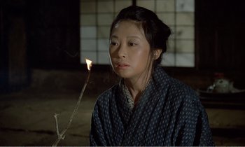Movie still from “Empire of Passion” (1978), directed by Nagisa Ôshima – A young woman holding a stick with a lit candle in front of her face; Medium shot, High angle