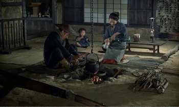 Movie still from “Empire of Passion” (1978), directed by Nagisa Ôshima – Three people sitting around a fire in a room; Wide shot, High angle