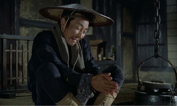 Movie still from “Empire of Passion” (1978), directed by Nagisa Ôshima – A man sitting down wearing an asian hat; Medium shot, High angle