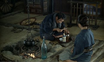Movie still from “Empire of Passion” (1978), directed by Nagisa Ôshima – A man sitting on the ground with a plate of food in front of him; Wide shot, High angle