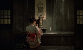 Movie still from “Empire of Passion” (1978), directed by Nagisa Ôshima – A woman sitting in front of an altar with a candle; Wide shot, High angle