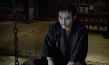 Movie still from “Empire of Passion” (1978), directed by Nagisa Ôshima – A man sitting on the ground with a white face mask on; Medium shot, High angle