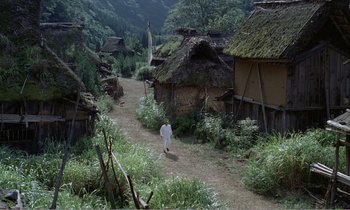 Movie still from “Empire of Passion” (1978), directed by Nagisa Ôshima – A man walking down a dirt path in front of some houses; Extreme Wide shot, High angle