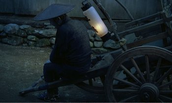 Movie still from “Empire of Passion” (1978), directed by Nagisa Ôshima – A man sitting on a cart with a lamp attached to it; Wide shot, High angle