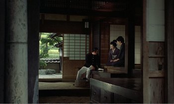 Movie still from “Empire of Passion” (1978), directed by Nagisa Ôshima – Three people sitting on a bench in a room; Wide shot, High angle