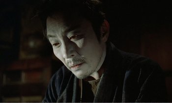 Movie still from “Empire of Passion” (1978), directed by Nagisa Ôshima – A man in a black robe with white makeup; Close Up shot, High angle