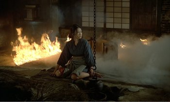 Movie still from “Empire of Passion” (1978), directed by Nagisa Ôshima – A woman sitting on the ground in front of a fire pit; Wide shot, High angle