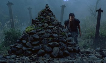 Movie still from “Empire of Passion” (1978), directed by Nagisa Ôshima – A man standing next to a large pile of rocks; Wide shot, Low angle