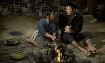 Movie still from “Empire of Passion” (1978), directed by Nagisa Ôshima – A man and a woman sitting on the ground near a fire pit; Medium shot, High angle