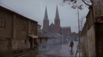 Movie still from “Empire of the Sun” (1987), directed by Steven Spielberg – People walking down a street in front of a church; Extreme Wide shot, Low angle