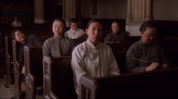 Movie still from “Empire of the Sun” (1987), directed by Steven Spielberg – A group of people sitting in a row of pews; Medium shot, High angle