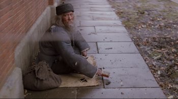 Movie still from “Empire of the Sun” (1987), directed by Steven Spielberg – An old man sitting on the side of the street; Wide shot, High angle