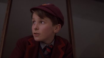 Movie still from “Empire of the Sun” (1987), directed by Steven Spielberg – A young boy wearing a maroon jacket and a red hat; Close Up shot, Low angle