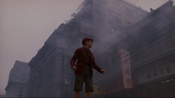 Movie still from “Empire of the Sun” (1987), directed by Steven Spielberg – A man standing in front of a tall building in the fog; Wide shot, High angle