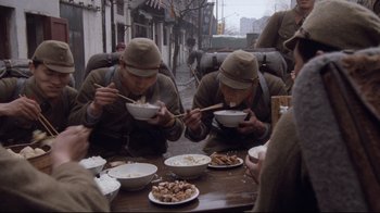 Movie still from “Empire of the Sun” (1987), directed by Steven Spielberg – A group of men eating food at an outdoor table; Wide shot, High angle
